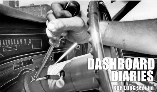 Black & white photo of a man's arm hot-wiring a vintage car steering column